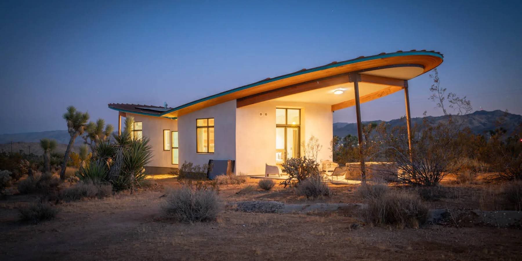 Mesa Sky Disk, a strawbale short-term rental structure in the Mojave desert, lit from within at dusk.